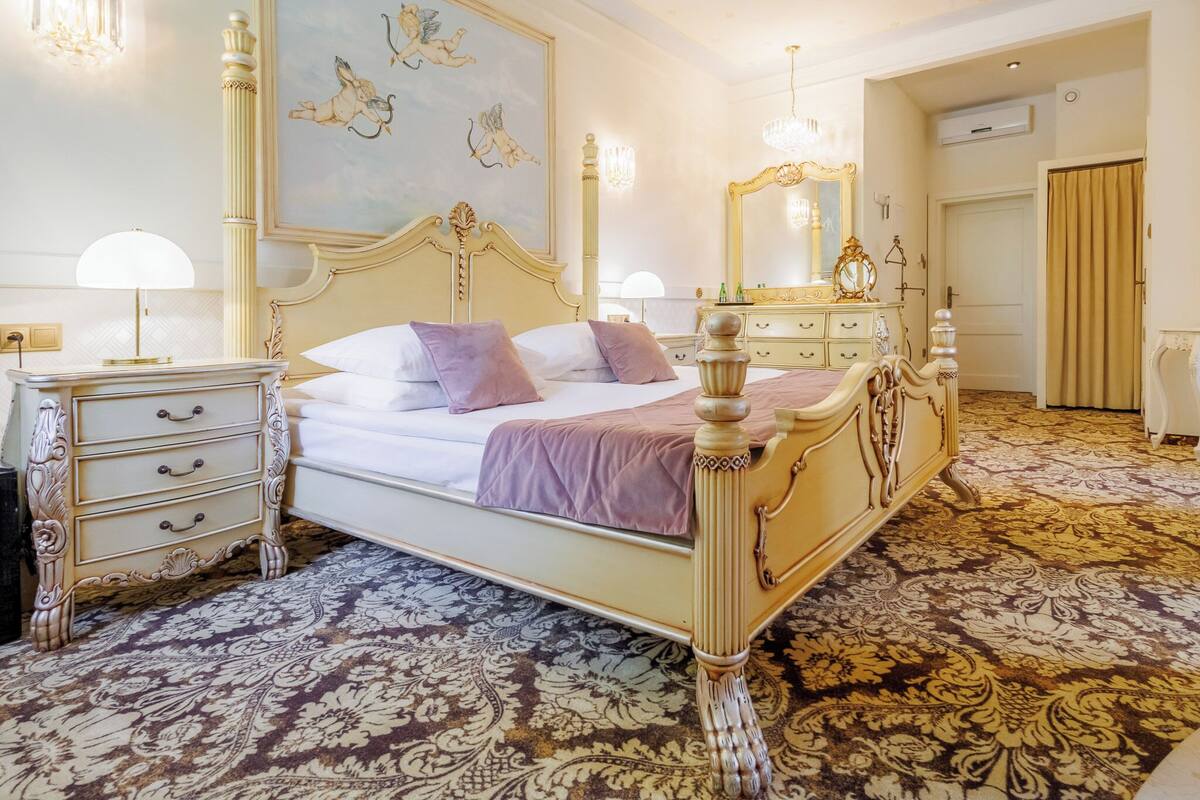 Une chambre classique, élégamment meublée, avec un grand lit, une commode richement décorée et un miroir ornemental.