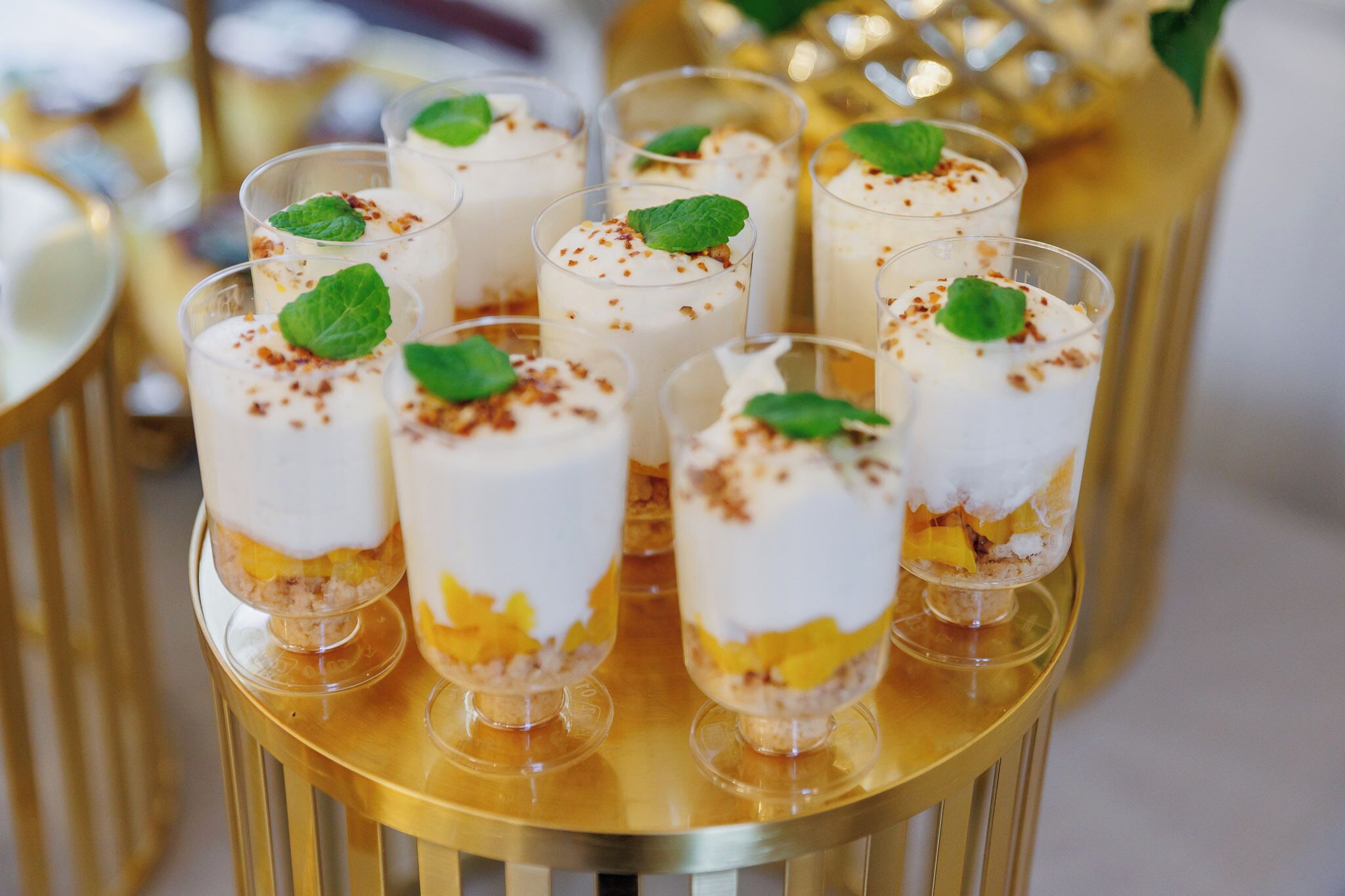 Une série de coupes à dessert garnies de crème fouettée et de fruits, décorées de feuilles de menthe, disposées sur un plateau doré.