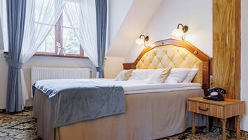 Ein ordentlich bezogenes Bett mit Kopfteil, ein Nachttisch mit Lampe und ein Fenster mit leichtem Vorhang.