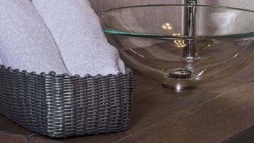 A bathroom with a glass bowl sink and a wicker basket with a towel.