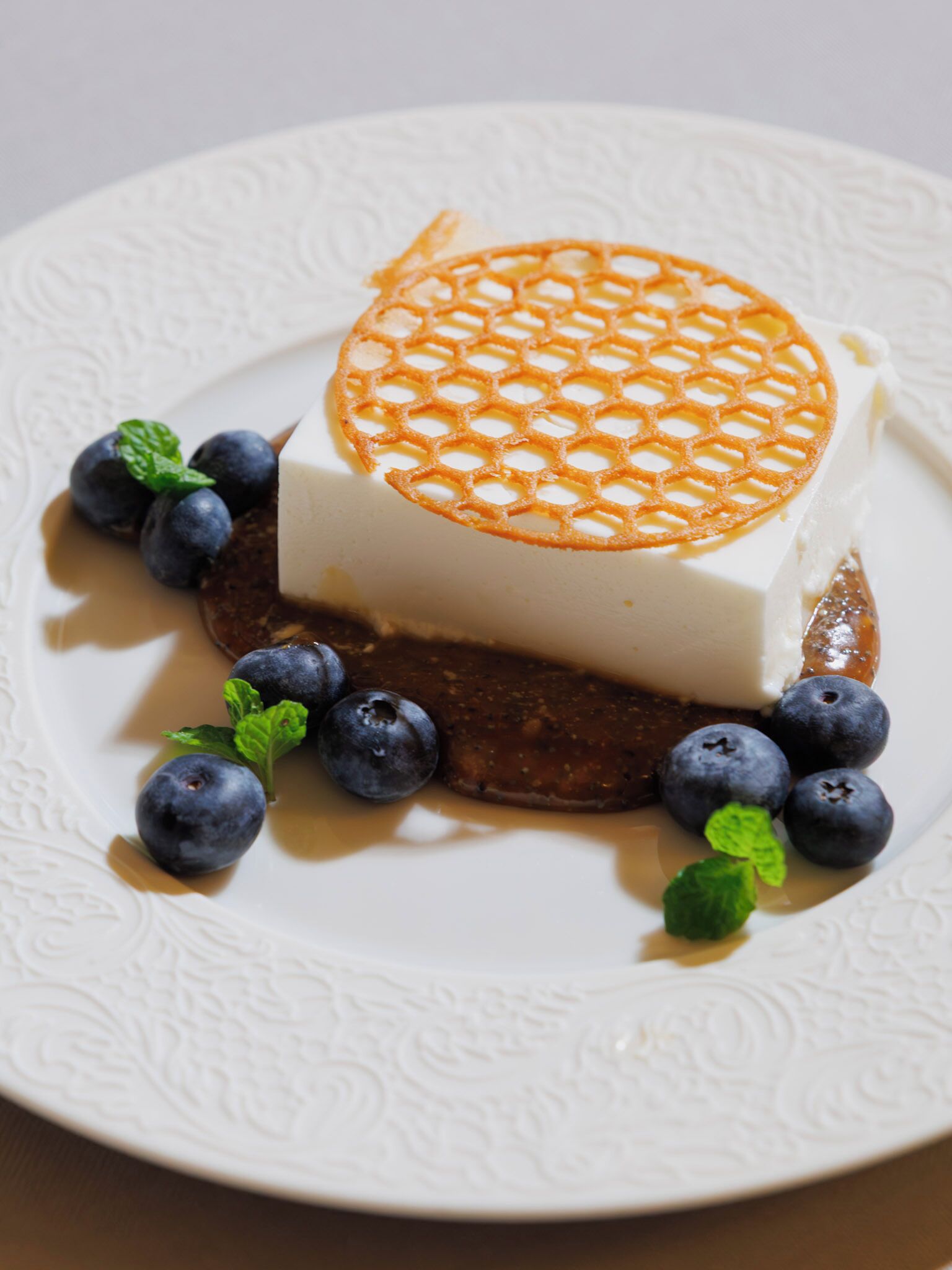 A dessert with a honeycomb top, blueberries, and mint leaves on a white plate.
