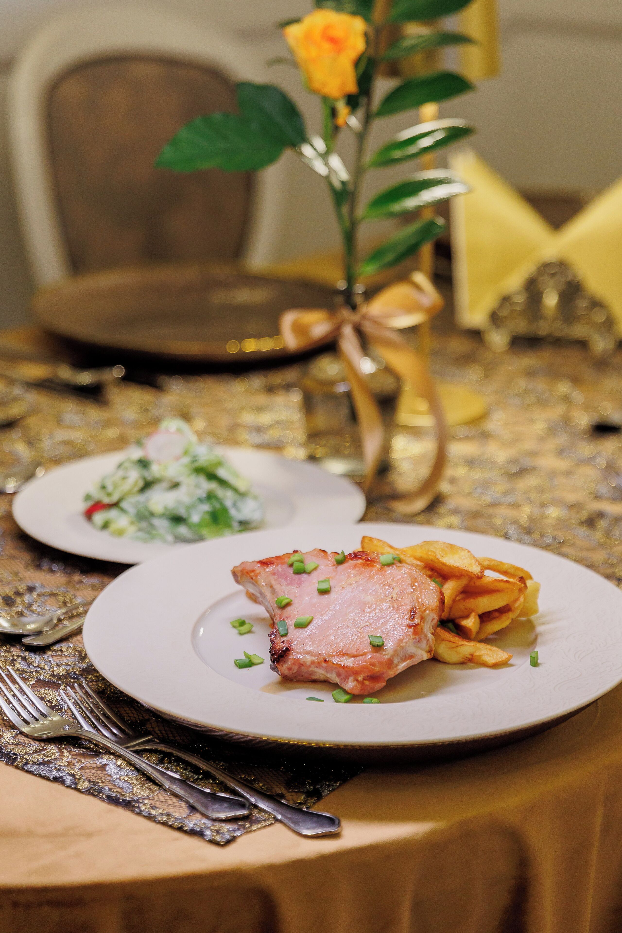 A dining table with plates of food, a vase with a yellow flower, and a gold decorative item.