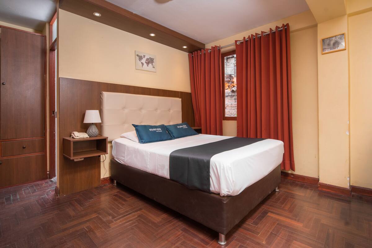 A bedroom with a large bed, wooden wardrobe, and a nightstand with a lamp.