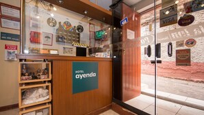 A hotel reception area with a wooden counter, a sign reading "HOTEL ayenda," and a glass door leading outside. - Ayenda Posada Inn (Cusco)