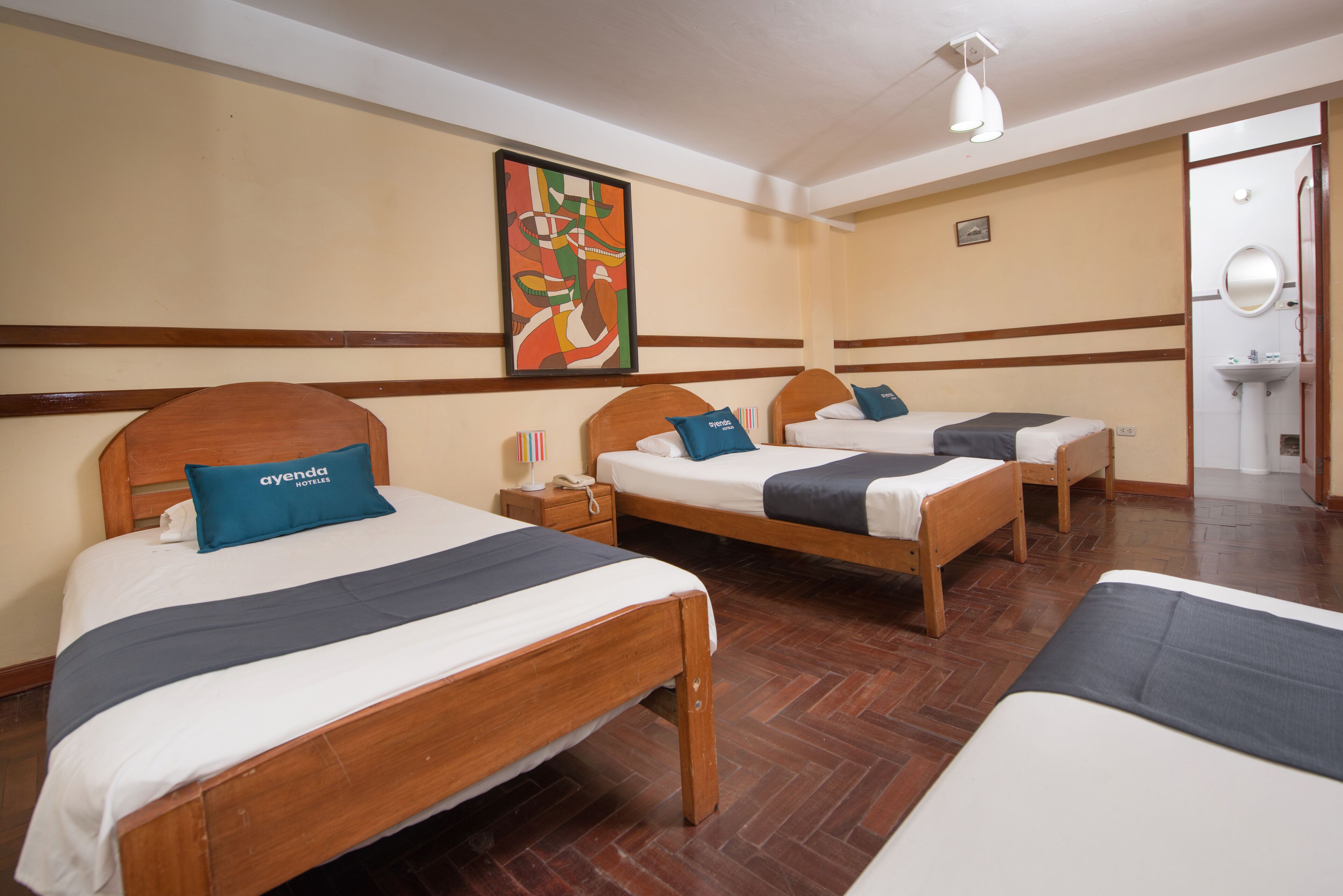 A hotel room with three wooden beds, each with a pillow and a blanket. There is a painting on the wall, a telephone, and a sink in the corner.