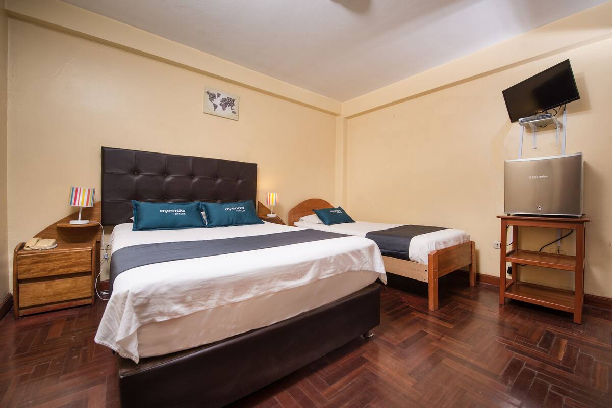 A hotel room with two beds, a flat-screen TV mounted on the wall, a wooden nightstand, and a desk with a laptop.