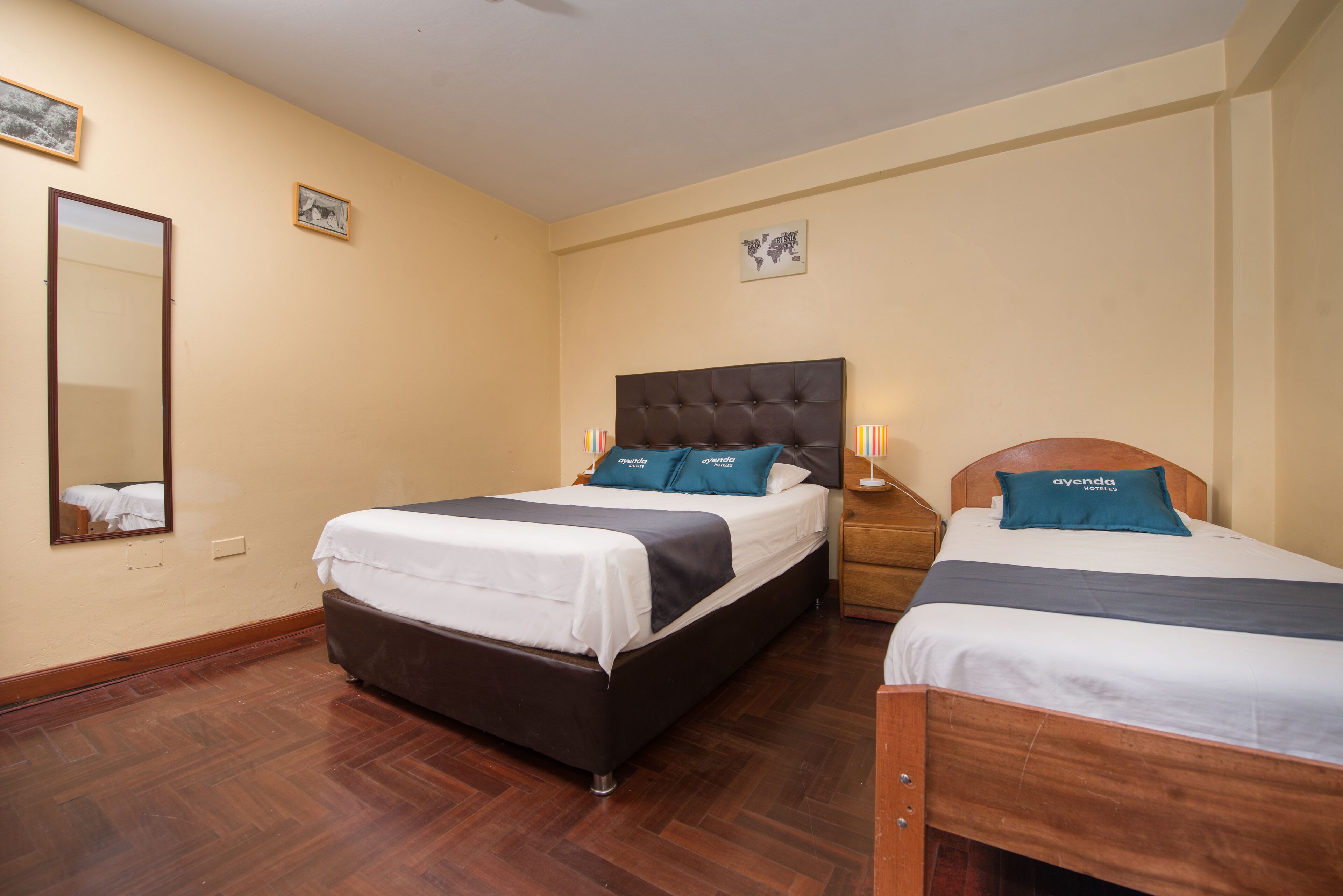 Habitación de hotel con dos camas, suelo de madera, un espejo grande y obras de arte colgadas en la pared.