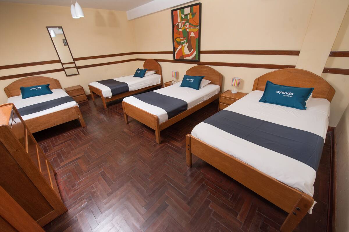 A hotel room with four single beds, wooden headboards, and a herringbone-patterned wooden floor.