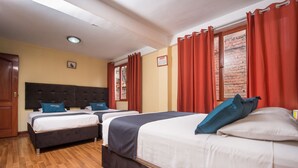 A hotel room with two beds, wooden flooring, red curtains, and a brick wall visible through the window. - Ayenda Posada Inn (Cusco)