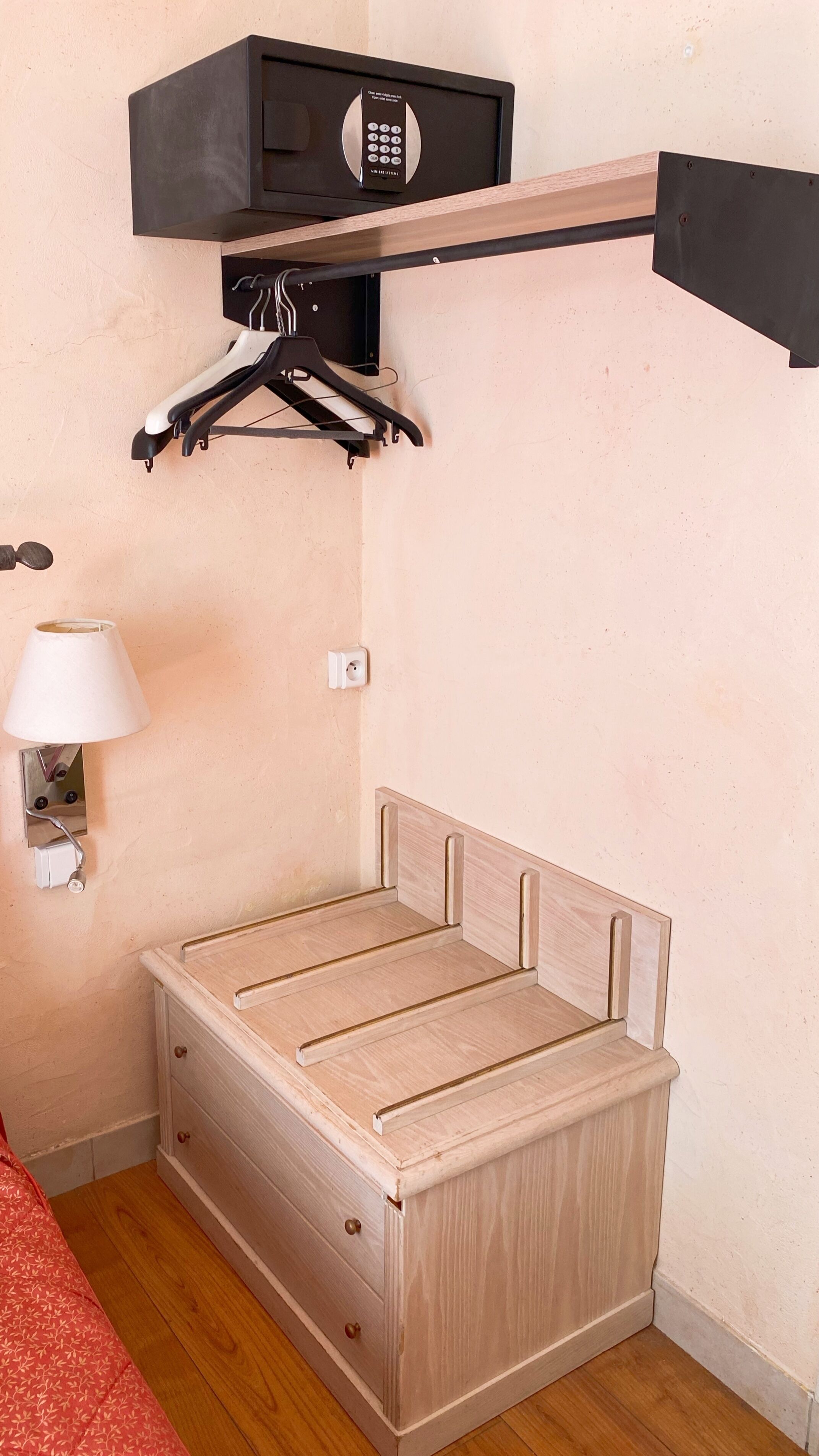 A compact room with a bed, a wall-mounted heater, a lamp, and a coat rack.