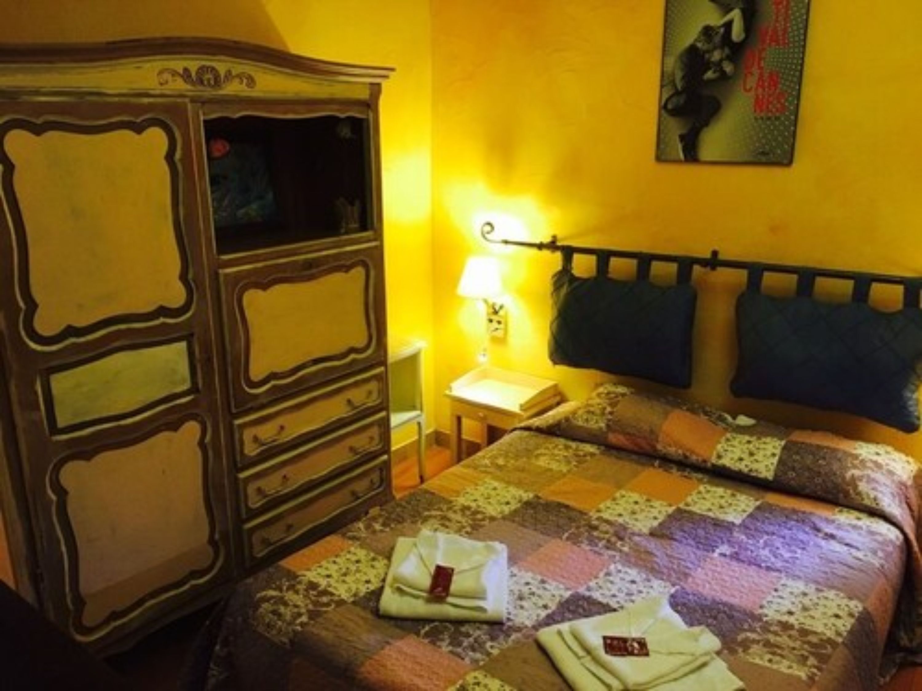 A bedroom with a bed, a dresser, a nightstand, and a wall-mounted lamp.