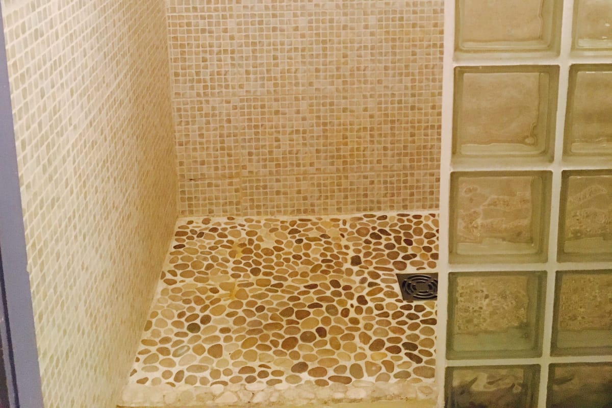 En dusch med väggar och golv beklädda med mosaik, en duschdörr i glas och ett duschmunstycke i metall.