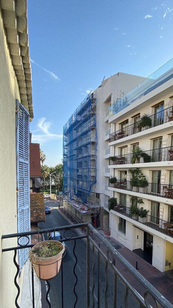 Vista de un edificio en construcción con andamios, una calle con un automóvil estacionado y un balcón con una maceta.