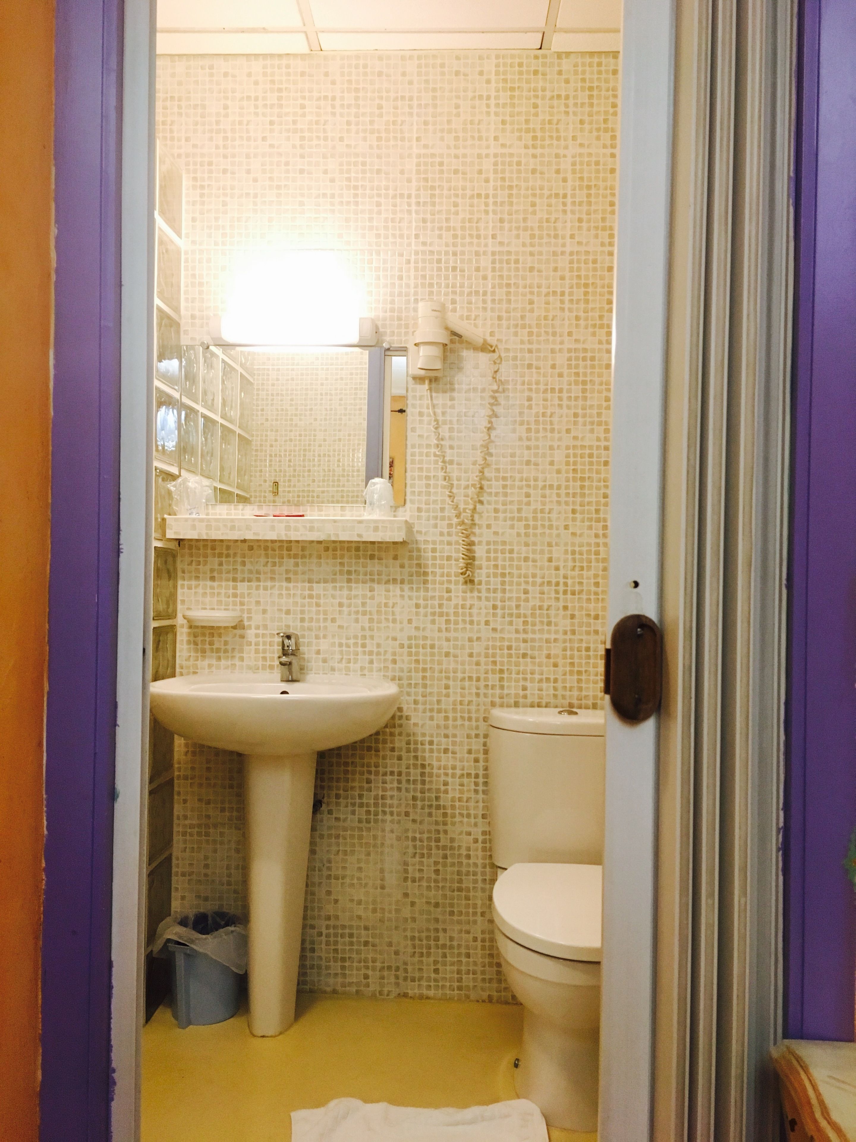 A bathroom with a tiled wall, a sink, a toilet, and a shower area.