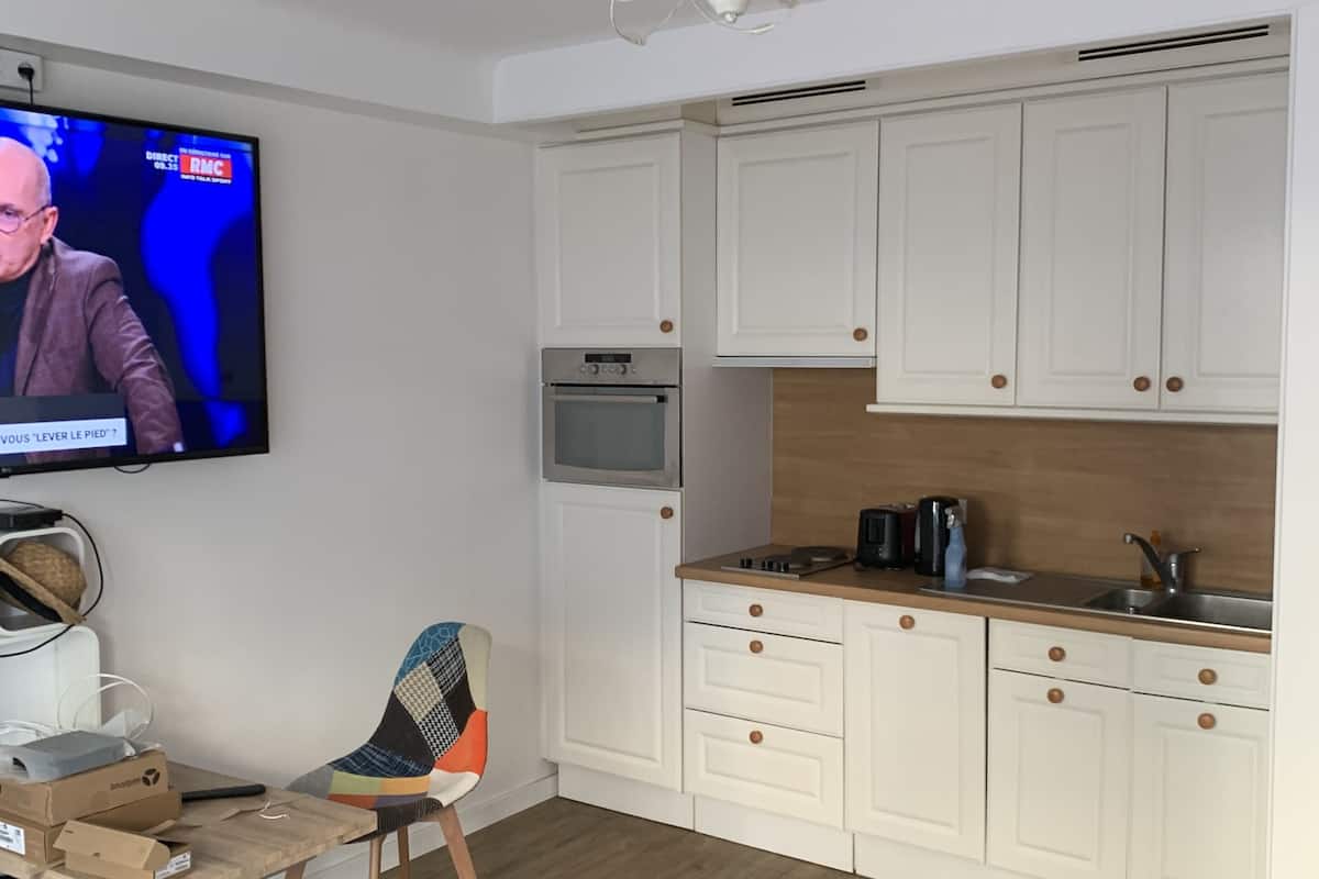 Ett modernt kök med vita skåp, en inbyggd ugn och en mikrovågsugn. Det finns ett matbord i trä med en färgglad stol och en tv som är monterad på väggen.