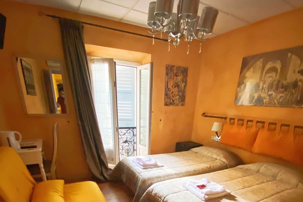 Ett hotellrum med två sängar, en stol, ett skrivbord, en kristallkrona och en balkong med utsikt.