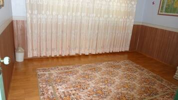 Habitación con alfombra de estampado floral, piso de madera, cortina con diseño de hojas y un pequeño bote de basura.