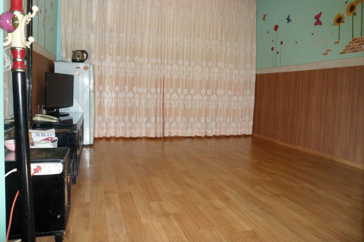 Une pièce avec un plancher en bois, un réfrigérateur blanc, une télévision et un rideau à motifs floraux.