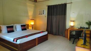 Quarto de hotel com cama, abajures, escrivaninha com computador e janela com cortinas.