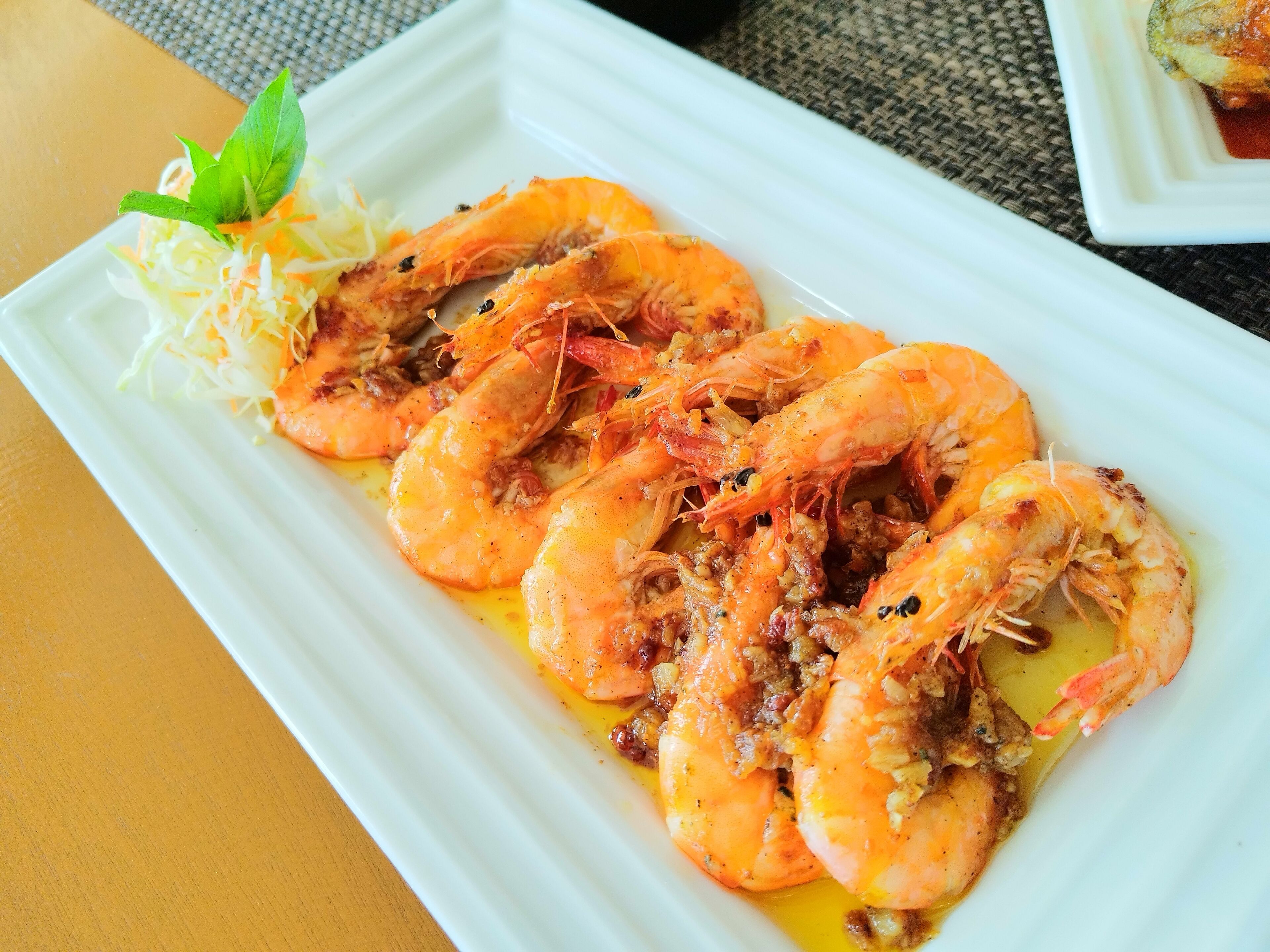 A white rectangular plate with cooked shrimp garnished with shredded vegetables and a small green leaf.