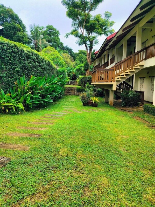 A lush garden with a pathway leading to a building with a wooden balcony. - Asia Grand View Hotel (Coron)
