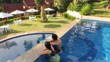Relax by the tranquil pool surrounded by lush greenery and traditional hotel buildings.