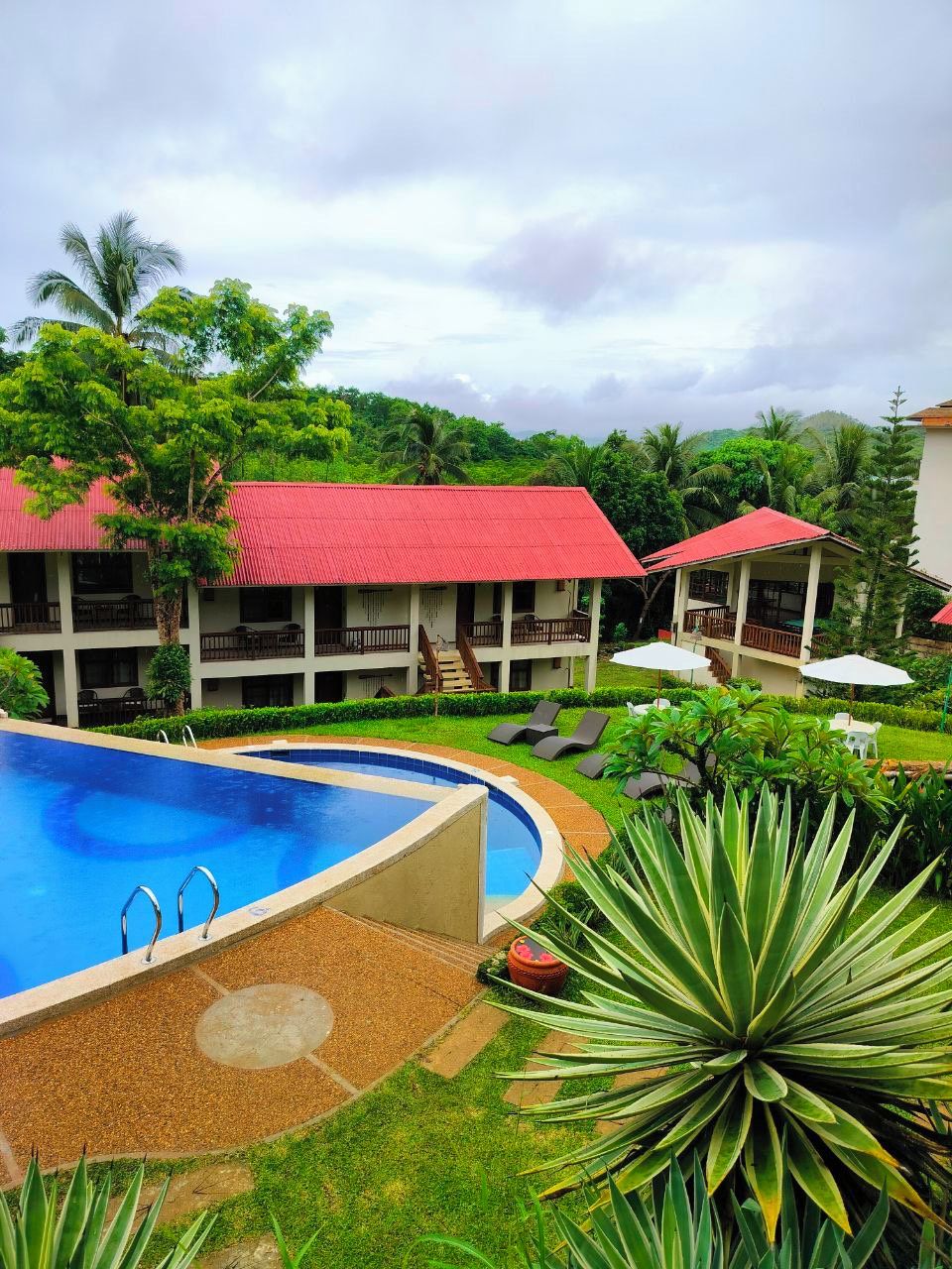 Un resort con piscina, sillas de descanso y un edificio de techo rojo.