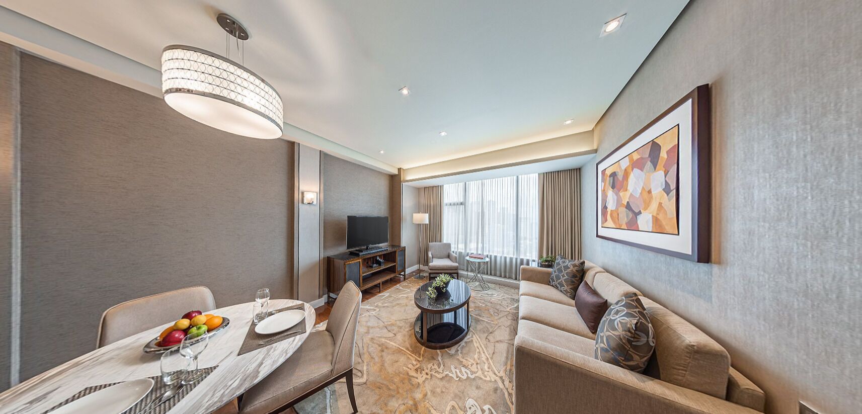 A modern hotel room with a dining area, a sofa, a television, and a large window.