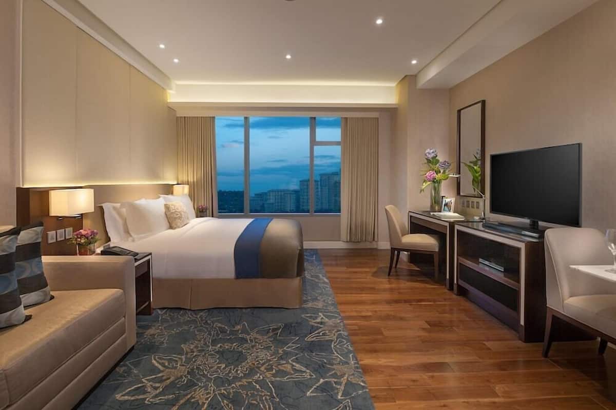 A hotel room with a large bed, a desk, a TV, and a view of the cityscape.