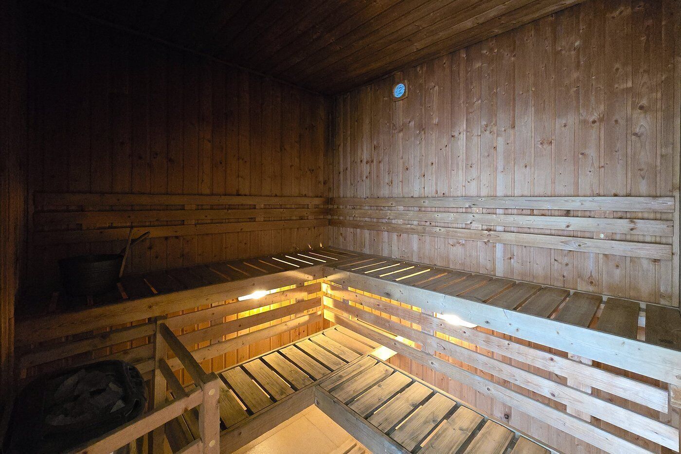A sauna with wooden benches and a visible clock on the wall.