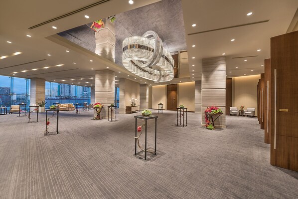 Un hall d’hôtel spacieux, doté de hauts plafonds, d’un grand lustre et de plusieurs espaces aménagés pour s’asseoir.