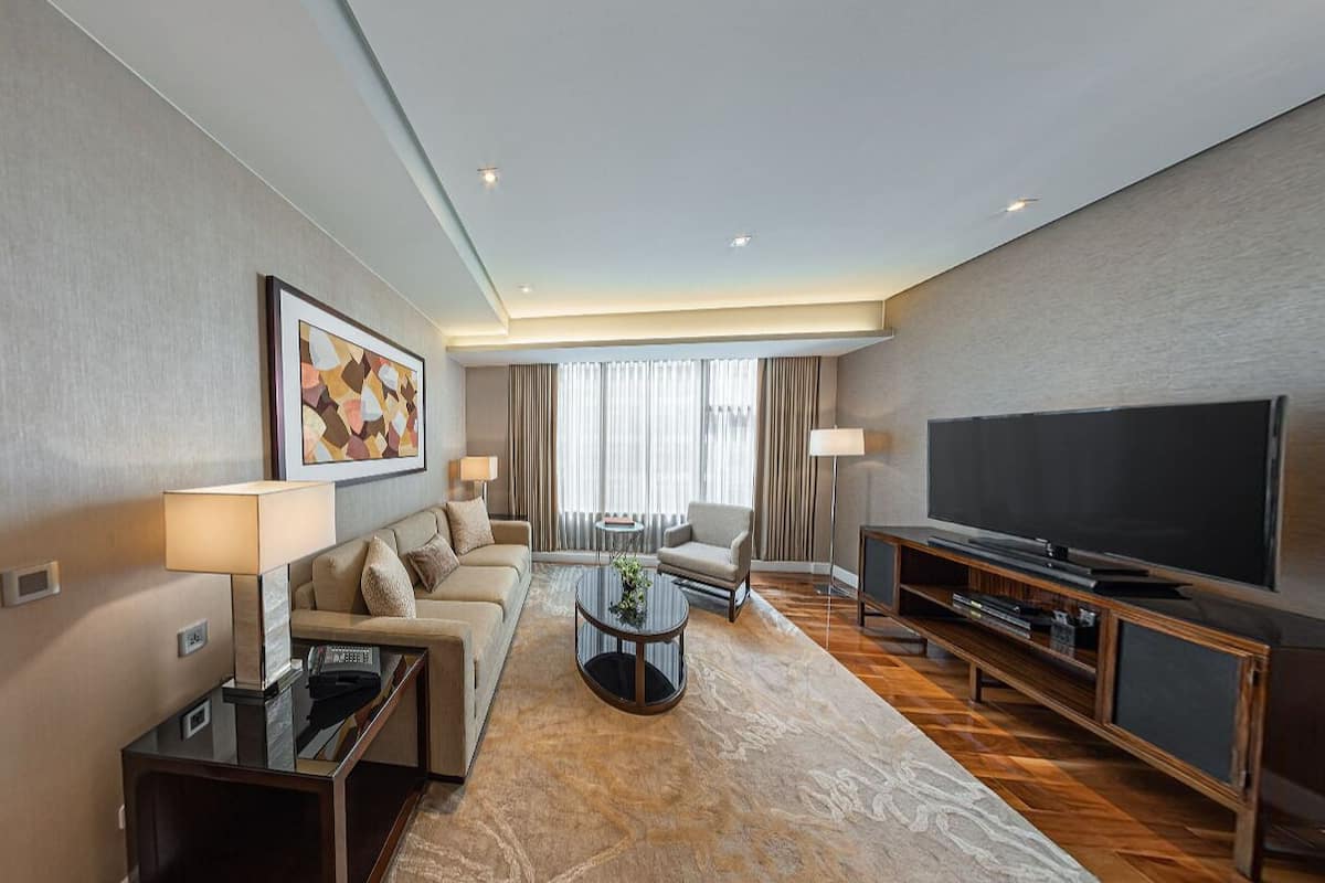 A hotel room with a sofa, coffee table, TV, and a dining area with a table and chairs.