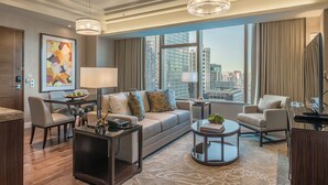 Una sala de estar moderna con sofá, sillones, una mesa de centro y un comedor. Amplios ventanales ofrecen vista a la ciudad.