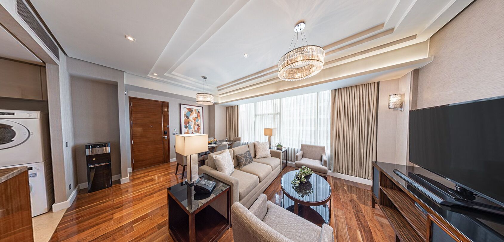 A hotel room with a living area, a television, a coffee table, a sofa, a lamp, and a chandelier.