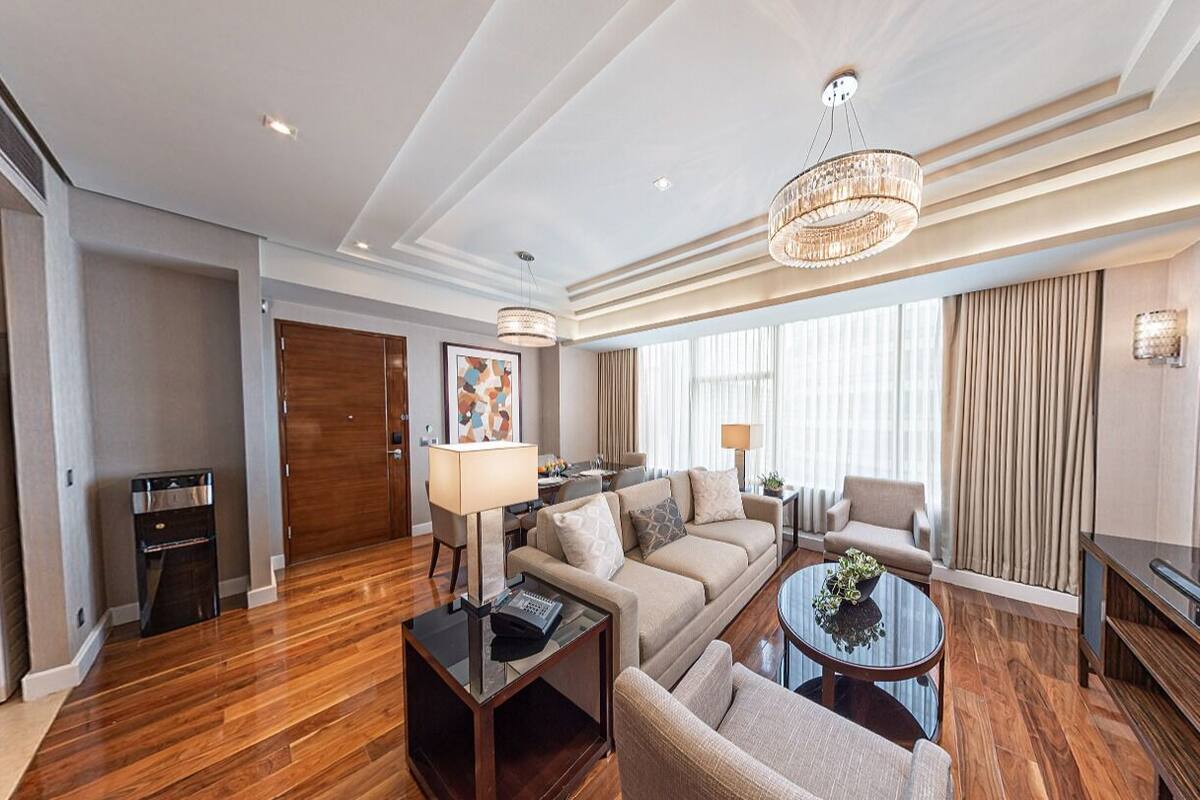 A hotel room with a living area, a television, a coffee table, a sofa, a lamp, and a chandelier.