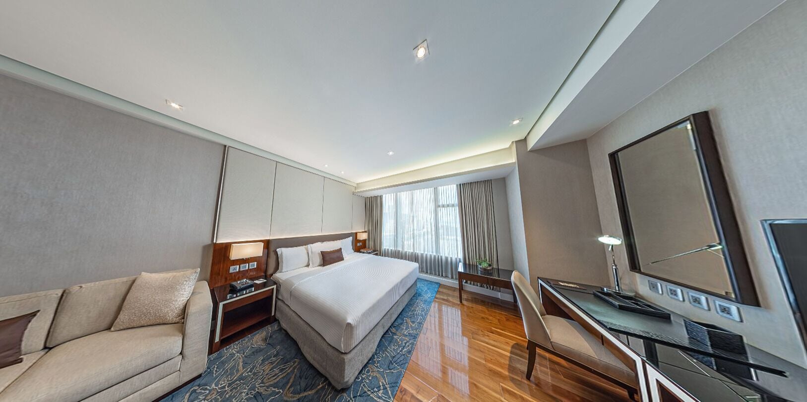A modern hotel room with a large bed, a desk, a TV, and a sofa.