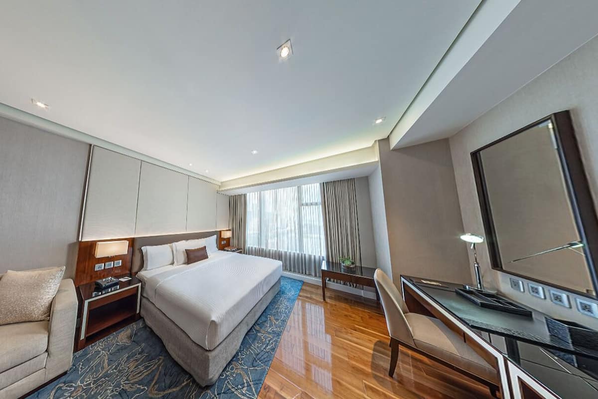A modern hotel room with a large bed, a desk, a TV, and a sofa.
