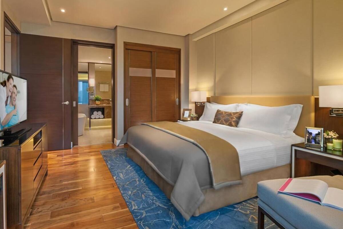 A hotel room with a large bed, a desk with a computer, a television, and a bathroom visible through an open door.