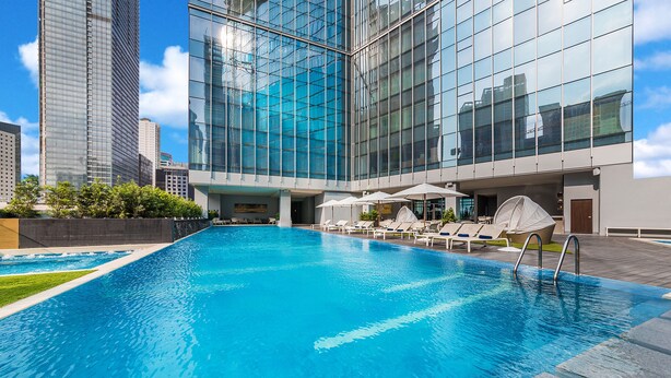 Un hotel moderno con piscina, sillas de descanso y vistas a edificios altos.