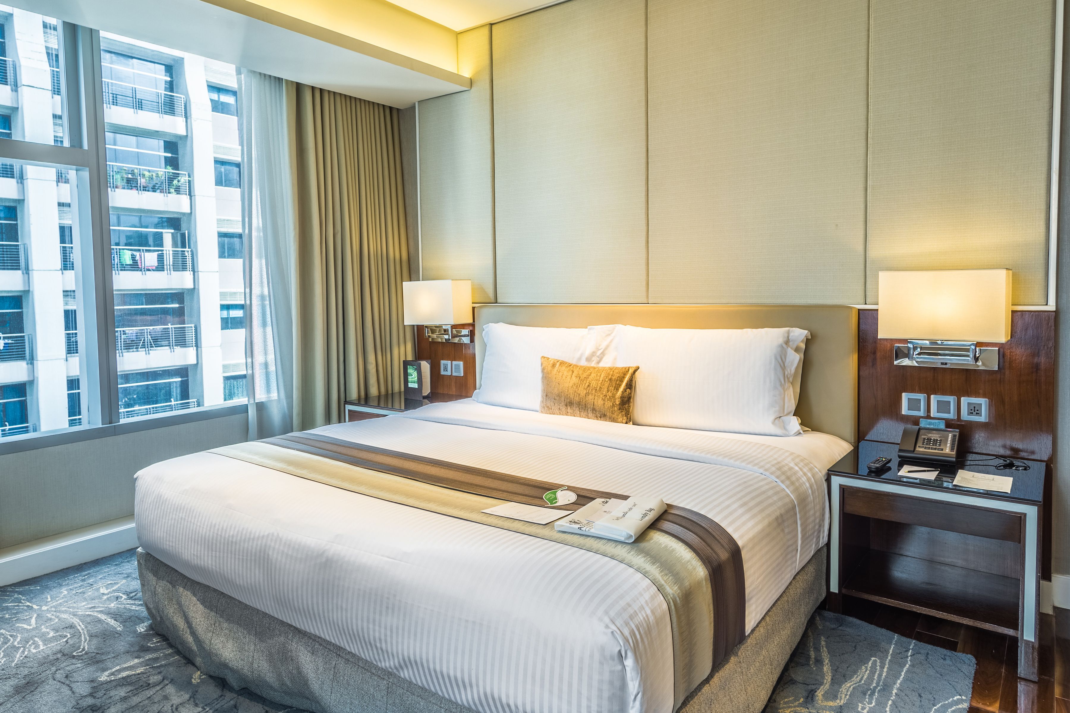 A hotel room with a large bed, two bedside tables, a window with curtains, and a view of a building.