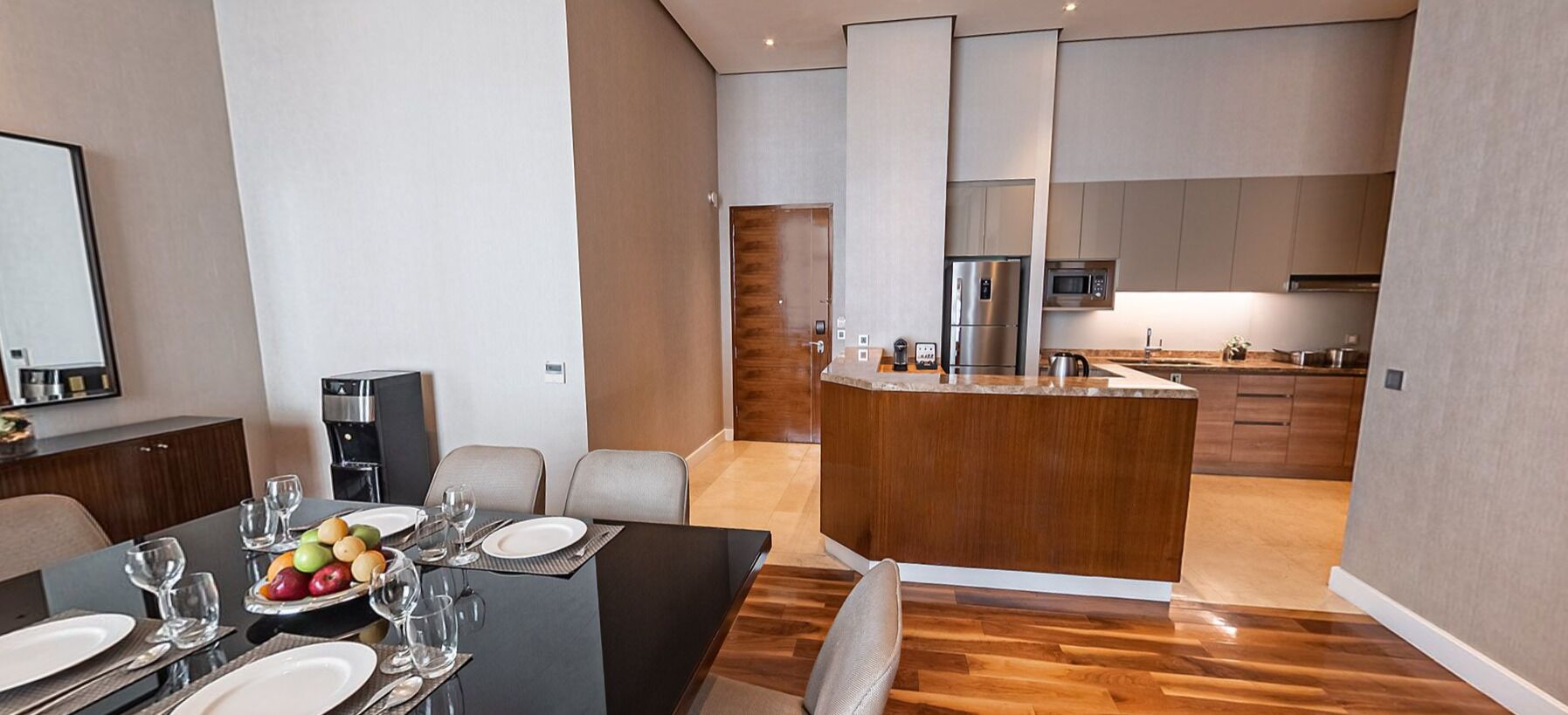 Una cocina moderna con una isla central, una zona de comedor con una mesa para dos, y otra zona de comedor con un ventanal grande.