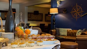 Una mesa de buffet con diversos alimentos, un jarrón grande y una decoración mural con forma de brújula en una habitación con un sofá de cuero marrón y una lámpara.
