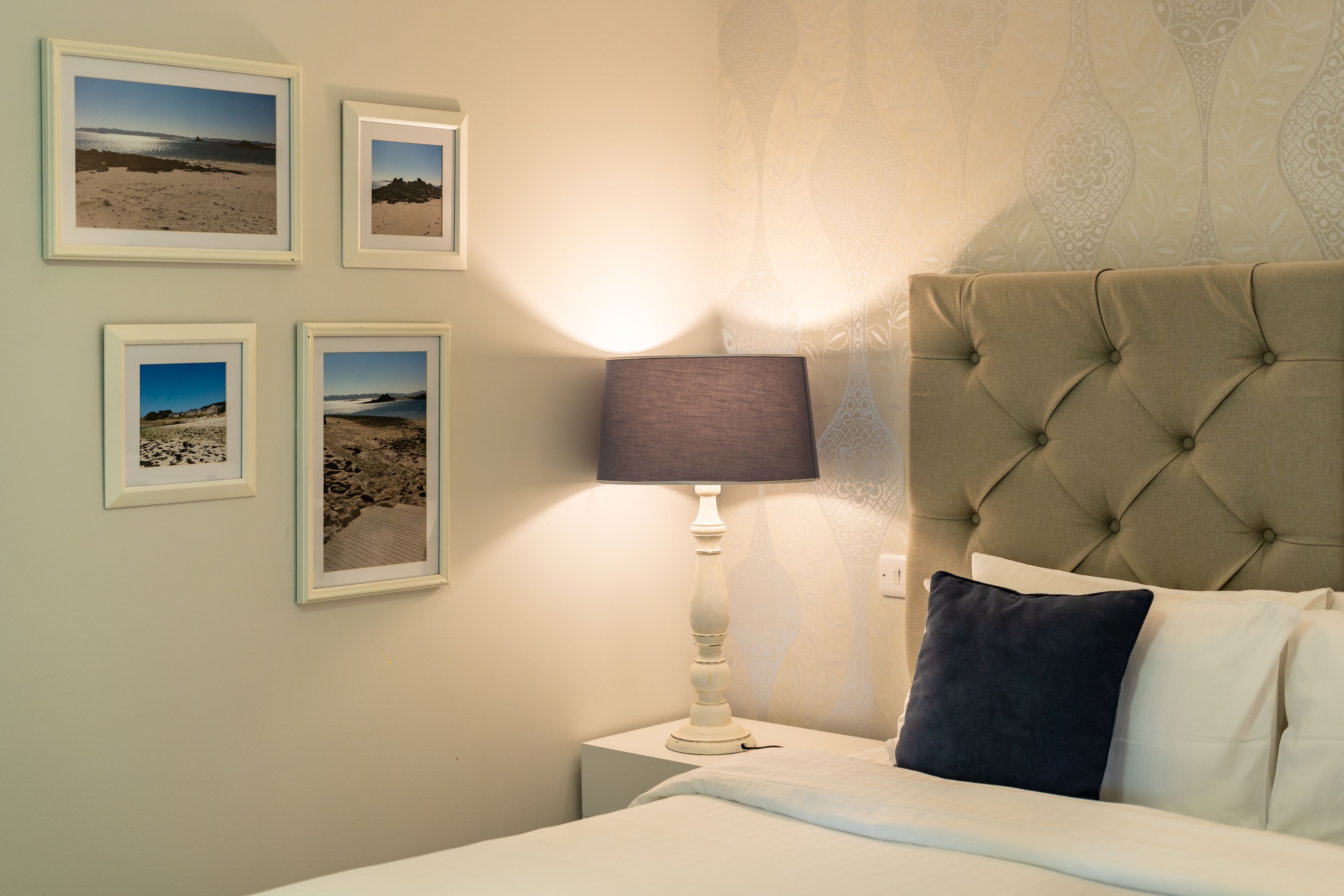 A bedroom with a bed, a nightstand, a lamp, and four framed pictures on the wall.