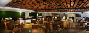 Un restaurante con mesas y sillas de madera, una zona de bar y una pared verde.