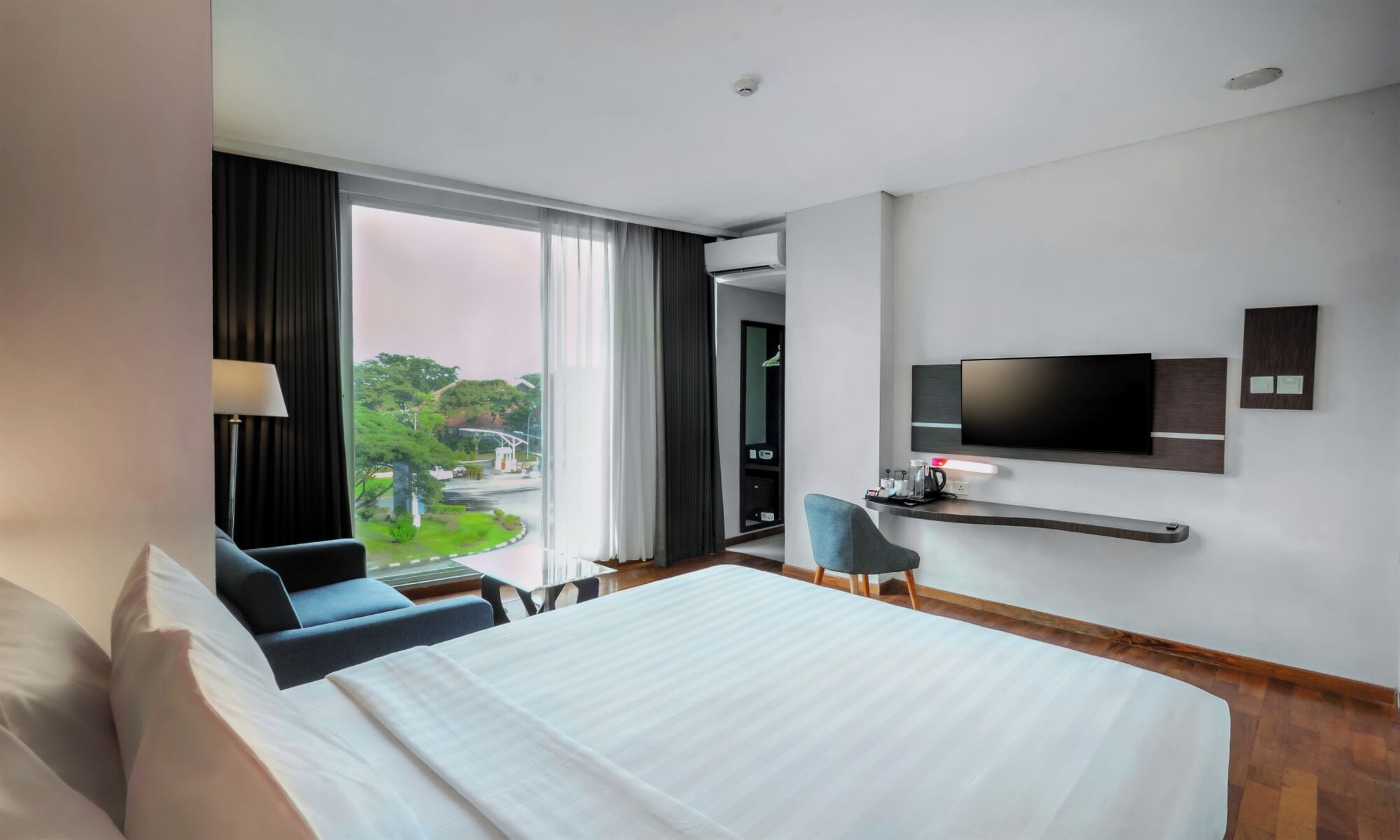 Habitación de hotel con cama, escritorio, silla, televisor y ventana con cortinas.