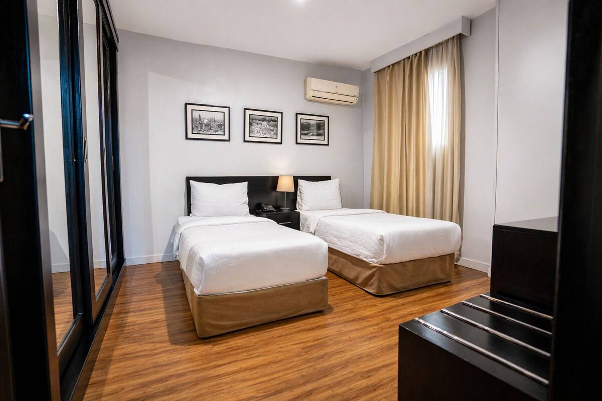 A hotel room with two beds, a desk, a chair, a TV, and a window with curtains.