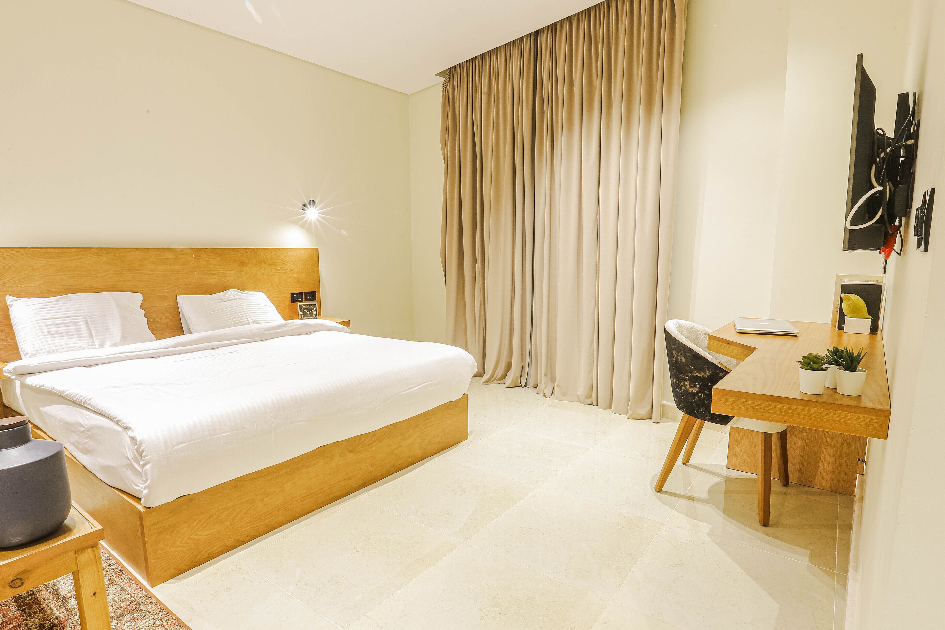 A hotel room with a bed, a desk, a chair, a lamp, a TV, and a curtain.