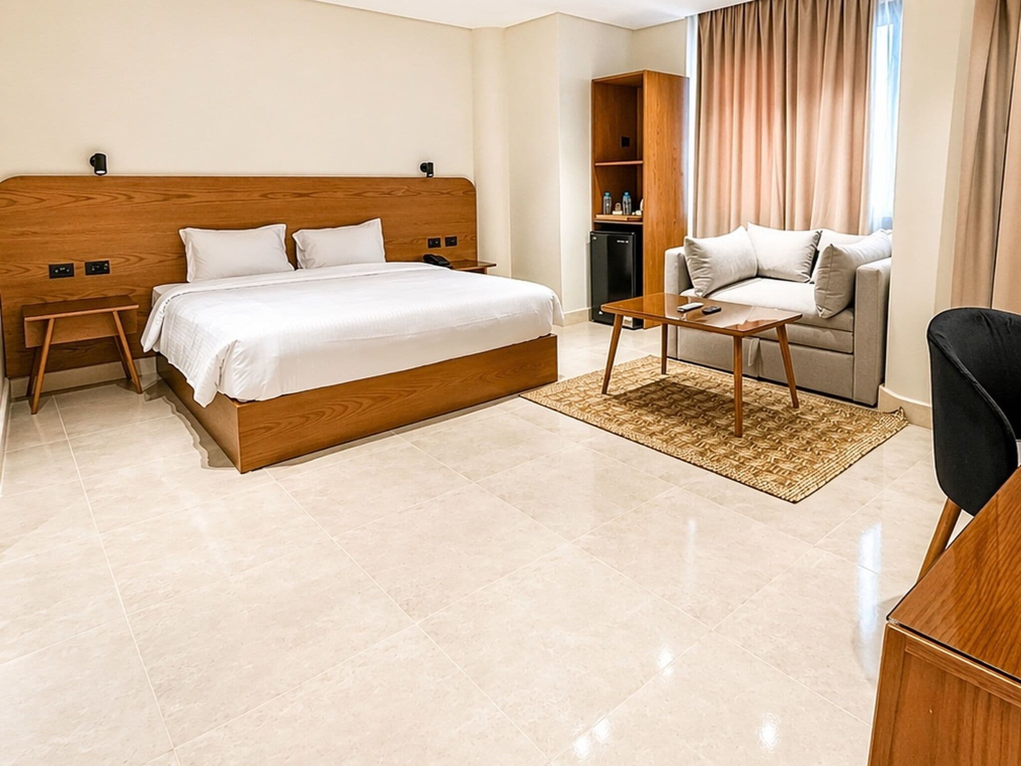 A hotel room with a wooden bed, a sofa, a coffee table, a TV, and a minibar.