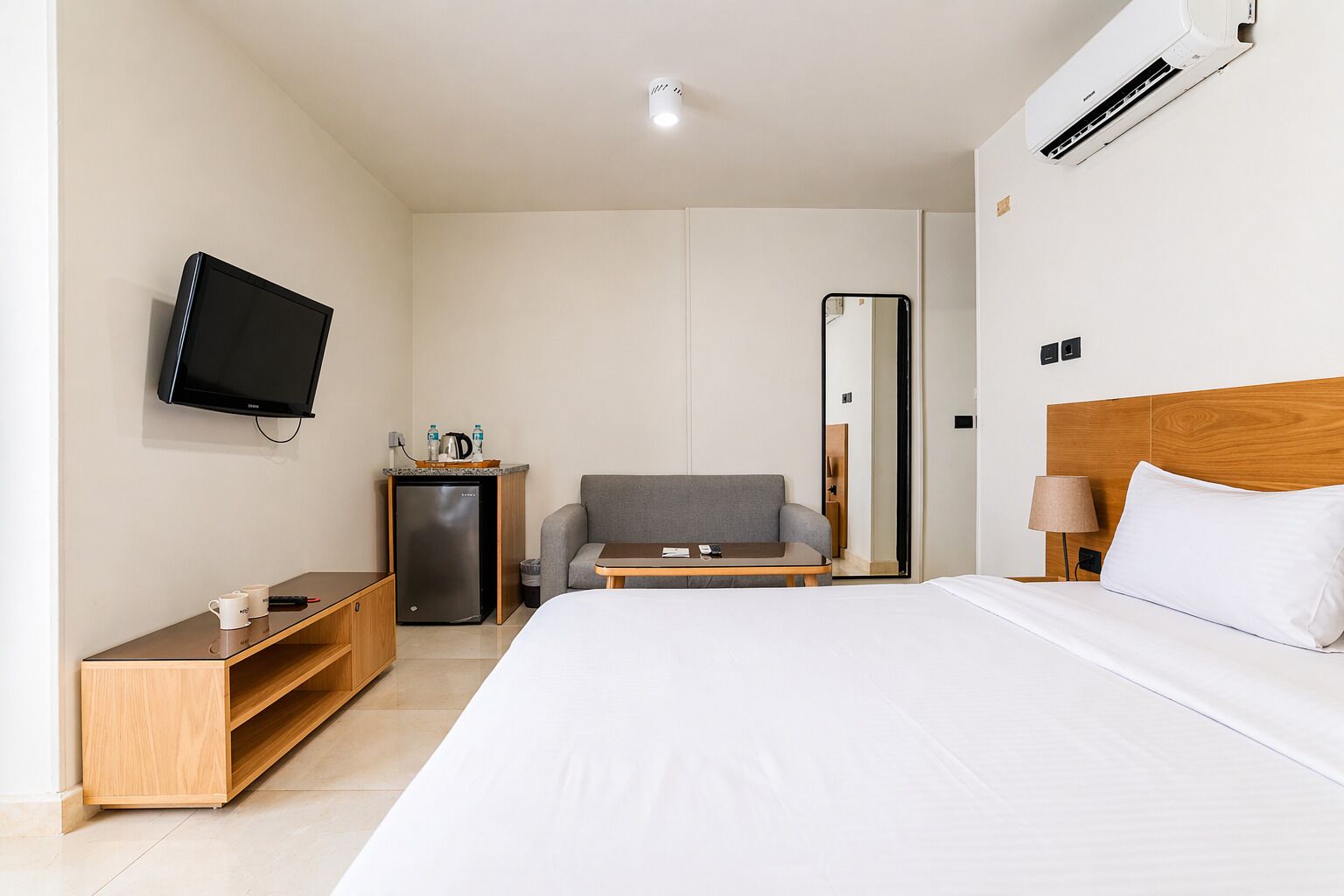 Ein Hotelzimmer mit Bett, Fernseher, kleinem Kühlschrank, Sofa, Tisch und Spiegel.