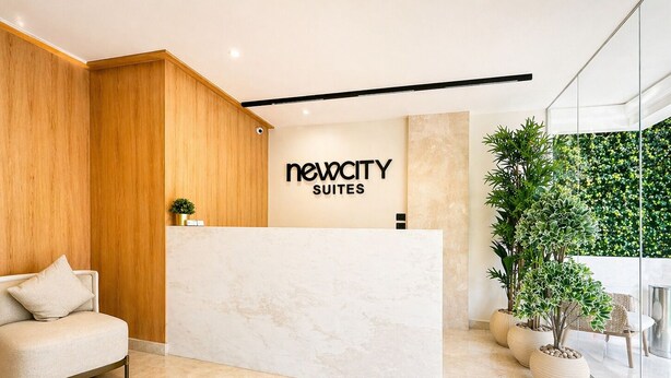 A reception desk with a sign reading 'Newacy Suites,' a seating area with a sofa, and potted plants. - NewCity Hotel & Suites (New Cairo)
